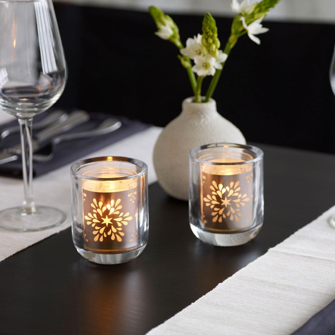 Ein eleganter, schwarz-weiß gedeckter Tisch in einem Restaurant. Auf dem Tisch stehen große Weingläser, eine kleine Steinvase mit ein paar weißen Blumen darin, sowie zwei brennende Relight Moods Kerzen in einem runden Glashalter.